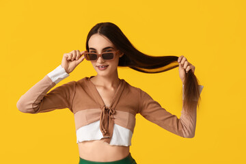 Obraz premium Beautiful young woman in stylish brown sunglasses on yellow background