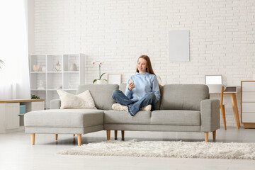 Fototapeta premium Young woman chatting with mobile phone on sofa in stylish living room