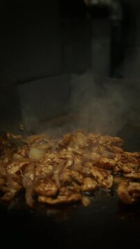 Close-up of chicken meat being cooked and stirred on a hot pan with spatula. Sizzling food and high heat cooking in professional kitchen. Steam rising and meat browning during cooking process.