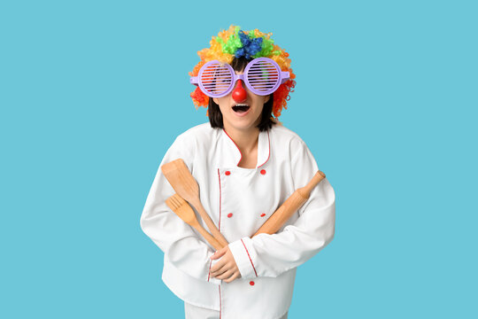 Funny young female chef with kitchen utensils on blue background. Fool's day