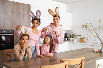 Happy family with bunny ears at table in kitchen on Easter Day