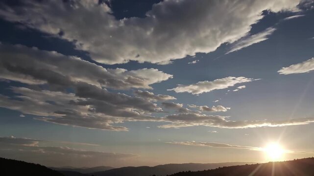 Serene Sunset over Mountainous Landscape with Dynamic Cloud Formations and Golden Sunburst Lighting Natural Scenery