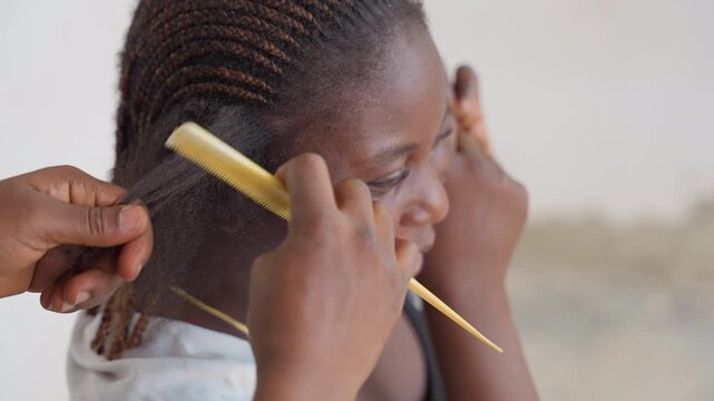 Closeup black woman hair being combed with yellow comb, hands working along cornrow roots, textured natural hair, warm relaxed smile, home setting, gentle scalp care and patient grooming by caregiver,