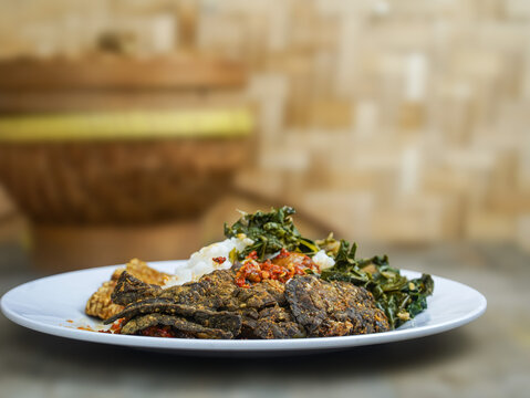 Delicious plate of nasi paru goreng with green vegetables and spices on a white plate in a traditional Indonesian setting with warm tones.