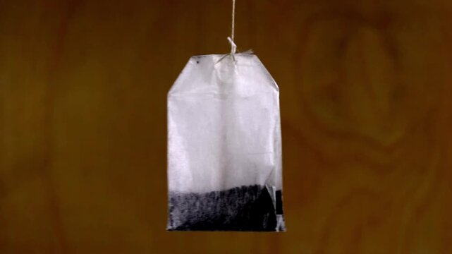 A tea bag on a rope hangs and sways in the wind against a dark wood texture background