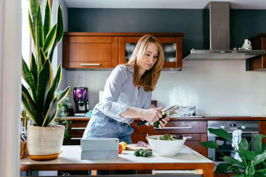 Caucasian woman in her 50s slicing vegetables and preparing salad in home kitchen