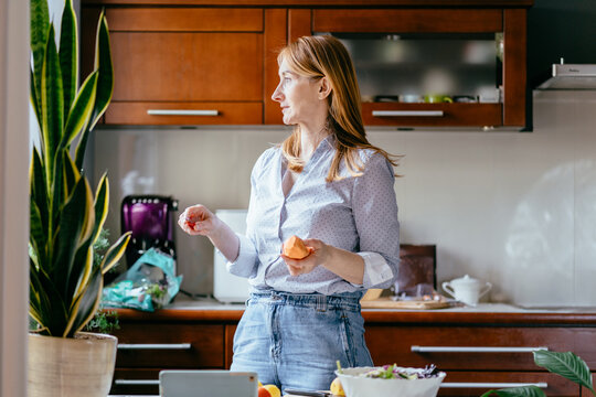 Caucasian woman in her 50s holding vegetables and thinking during cooking in kitchen