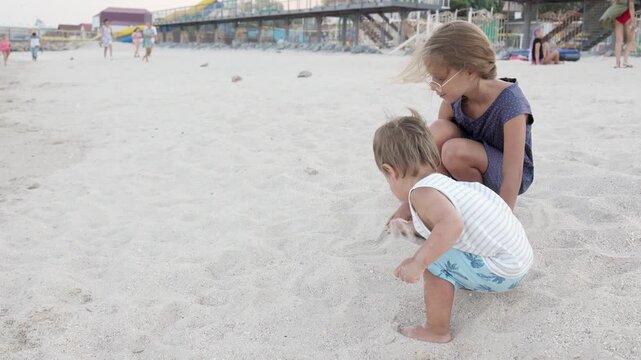 Girl helping her little brother to look for seashells in the sand on the coast