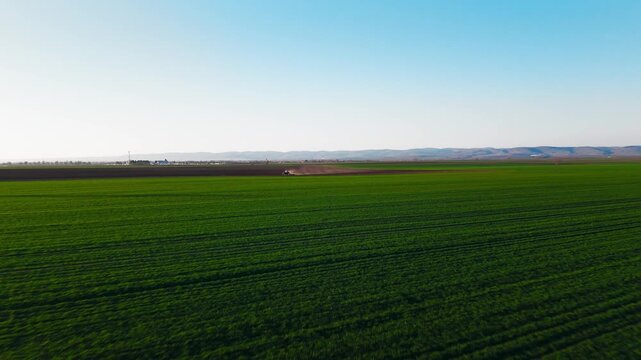 Aerial view of a lone tractor tilling the soil in a vast field, contrasting the dark earth with vibrant green crops, Jazak, Vojvodina, Serbia.