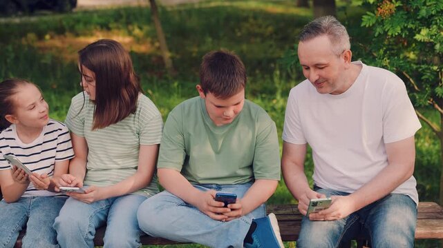 kids and adult on smartphones outdoors, children using mobile phones in a park, family screen time on a bench outside, preteens focused on smartphones in nature, kids browsing phones in a green garden