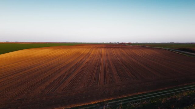 Aerial view of freshly plowed fields, casting long shadows under a warm sunset, contrasting with the green crops, Jazak, Vojvodina, Serbia.