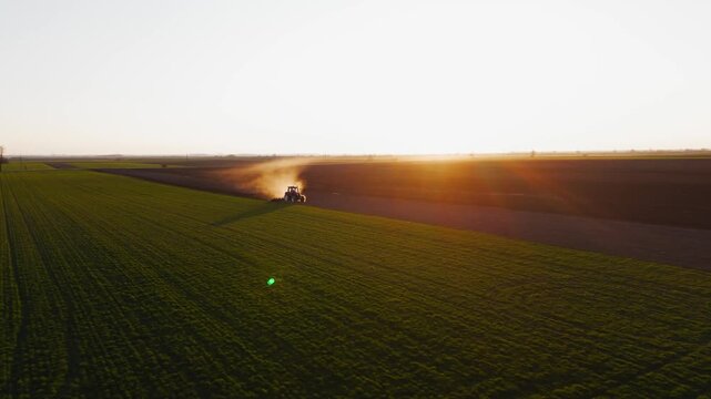 Aerial view of a tractor plowing a field, kicking up dust against the backdrop of the setting sun and a dark field, Jazak, Vojvodina, Serbia.