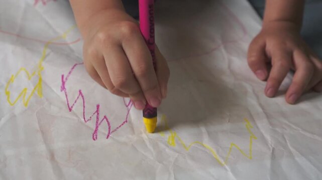 Close up of child's hand diligently drawing with a crayon, showcasing artistic expression on paper.