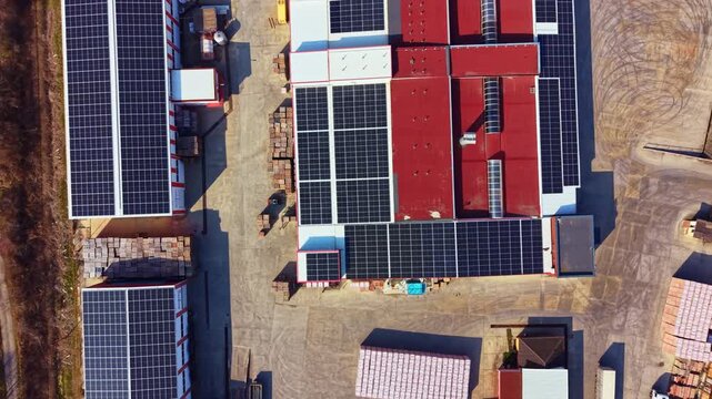 Rows of solar panels cover the roofs of several industrial buildings. The scene shows a clear sky above and the layout of the facility below during daylight hours.