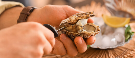 Young man opening fresh oyster with knife, closeup © Pixel-Shot