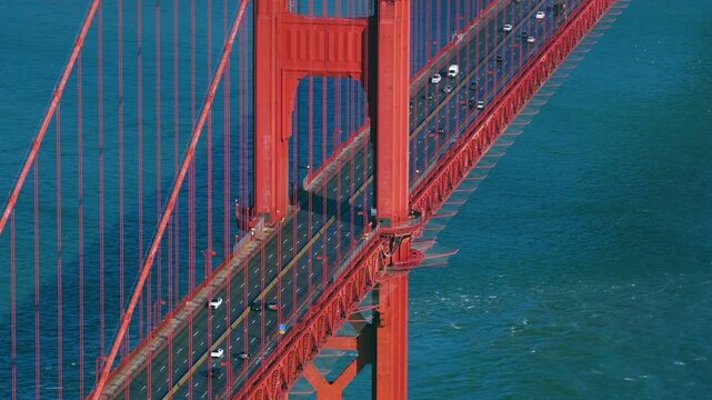 Traffic At Golden Gate Bridge With Its Iconic International Orange Tower And Suspension Cables Over Water. aerial arc shot