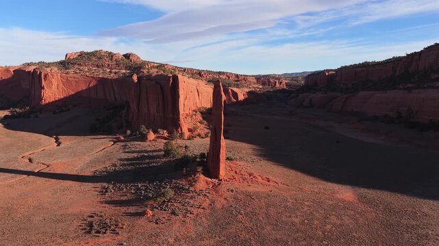 A smooth cinematic drone orbit circles an ancient stone needle spire, revealing the epic scale and mystical geological verticality within a legendary red rock fantasy desert landscape.