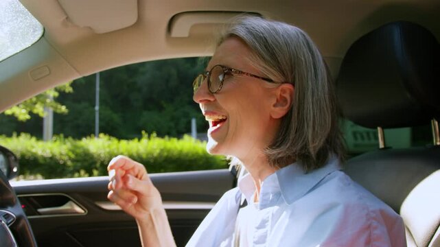 Happy Caucasian old woman driving car dancing singing song listening music inside automobile smiling retired senior aged female driver dance sing enjoying audio radio in auto drive granny having fun