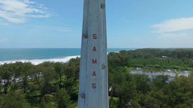 Aerial view of Mercusuar Samas lighthouse standing tall near the coast, contrasting with the blue sea and the lush green vegetation, Bantul Regency, Indonesia.