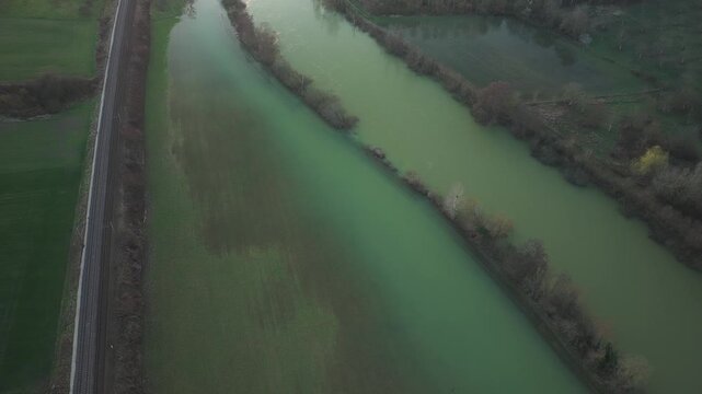 Aerial view of a river and parallel railway track cutting through fields and trees, creating textures, Courthiezy, Grand Est, France.