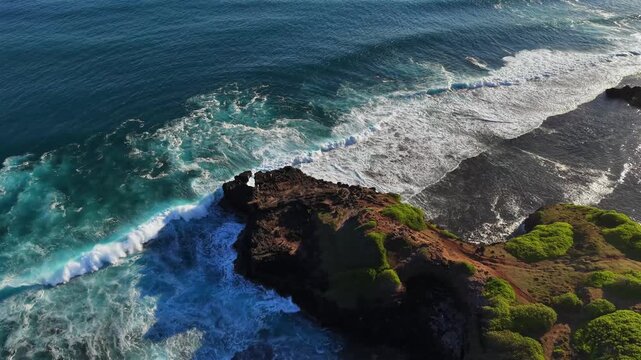 Vibrant turquoise waves crash against dark volcanic rock. White foam spills over moss-covered stone. Aerial perspective shows ocean's raw power. Ideal for travel or nature content