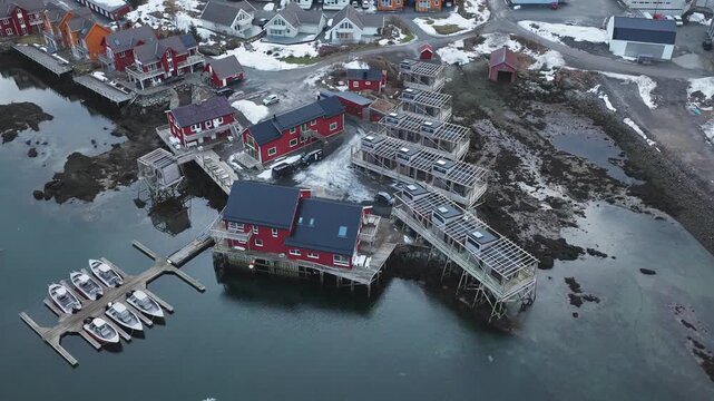 Aerial view of red houses dotting the landscape and boats docked on the water's edge, creating a striking contrast, Ballstad, Nordland, Norway.