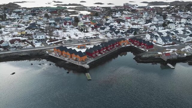Aerial view of the vibrant houses of Ballstad contrasting against the snowy landscape and dark sea, creating a striking visual harmony, Ballstad, Nordland, Norway.