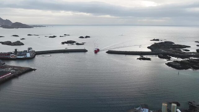 Aerial view of a red boat entering a harbor, its wake contrasting against the calm water, a picturesque scene, Ballstad, Nordland, Norway.
