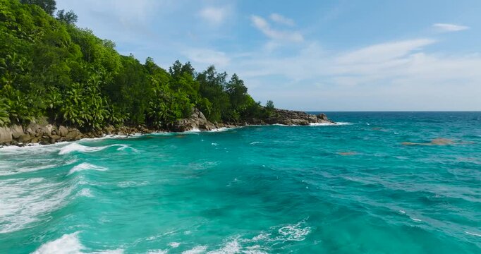 Coastal waves crashing against a rocky outcrop surrounded by lush tropical greenery. Seychelles, Mahe.