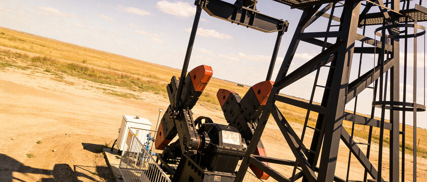 Angled view of base and counterweights of oil pump located on dry plain under bright daytime sky.