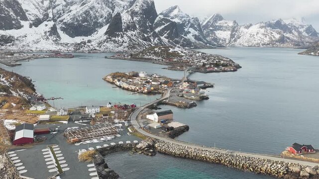 Aerial view of Hamn&oslash;y's quaint fishing village, with snow-capped mountains creating a striking contrast against the serene waters, Hamn&oslash;y, Nordland, Norway.