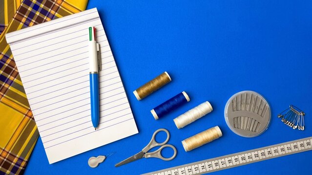A workbench with sewing tools: scissors, needles, pins, and a tape measure next to a notepad. Conceptual ideas for tailoring, clothing repair, and handicrafts.