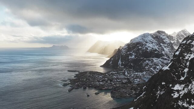 Aerial view of the dramatic Tind coastline where snow-capped mountains meet the moody ocean under the cloudy sky, Tind, Nordland, Norway.