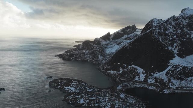 Aerial view of the Reinebringen mountain contrasting with the frigid waters and snow-dusted buildings in the Lofoten Islands, Reine, Nordland, Norway.