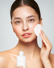 Young girl holds cotton pad while cleansing face with cosmetic milk. Skin care removal of makeup cleansing. Basic facial skin care