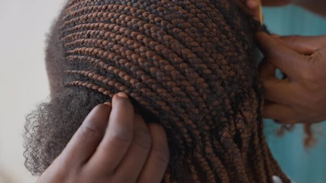 Closeup hands braiding hair, detailed cornrow pattern on scalp, stylist fingers weaving textured strands, salon atmosphere with focused craftsmanship, intimate tactile process showing precision