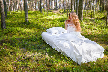 Woman wakes up in a summer forest. Young woman has breakfast in bed in a summer forest