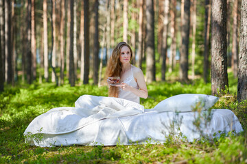Woman wakes up in a summer forest. Young woman has breakfast in bed in a summer forest