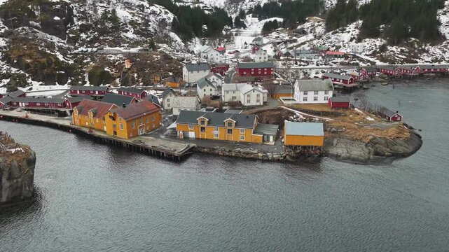 Aerial view of the quaint Nusfjord fishing village, where red and yellow wooden buildings contrast with the snow-dusted mountains, Nusfjord, Nordland, Norway.
