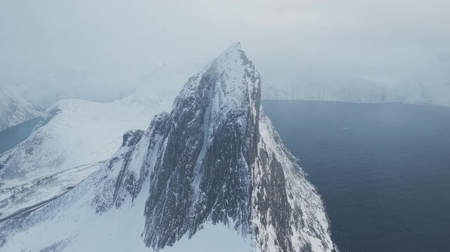 Aerial view of the snow-covered Segla mountain peak contrasting against the dark fjord waters creating a stunning winter landscape, Segla, Troms, Norway.
