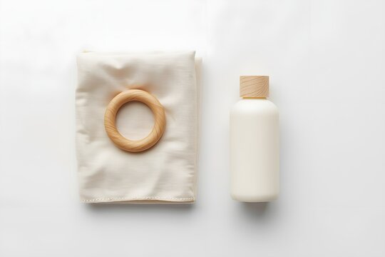Flat lay of a white bottle and cloth with a wooden teether on a clean white background.