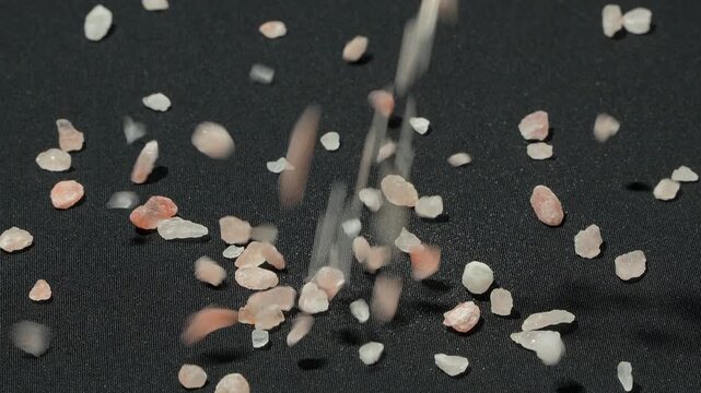 Slow motion action of pure pink Himalayan salt crystals falling on a black background. Premium natural mineral for healthy cooking and spa treatments.