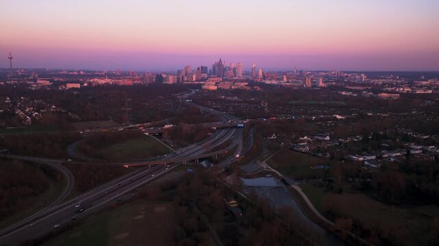 Aerial view of the Frankfurt skyline with a tower and buildings, contrasting with the surrounding greenery and roads during a dusky sunset, Frankfurt, Hessen, Germany.