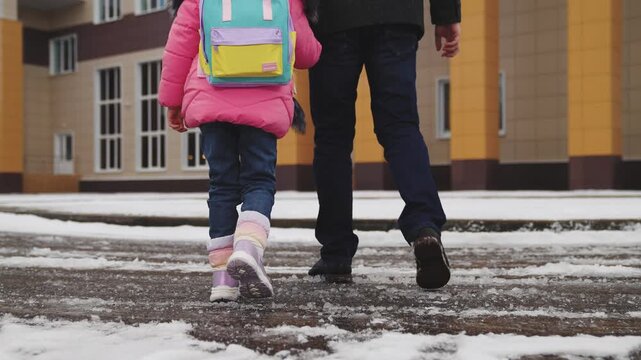 legs close-up, walking snow, child his father walk with their feet snow school building, child school backpack holds his father hand, little student goes class, parental support hand, cold snowy road