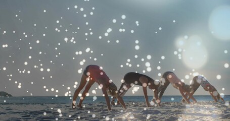 Naklejka premium Four women holding downward-dog on beach sunrise starting fitness flow as animated bokeh overlaying