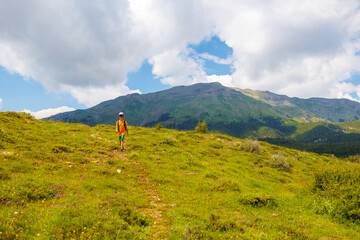 Obraz premium hiking in the mountains. A little boy with a backpack walks along a path against a background of mountains and clouds. Active healthy lifestyle on weekend hike journey.