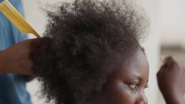 Closeup of woman caring for textured curls. Black woman gently combs coarse natural hair with care. Detailed closeup of stylist tenderly managing afro textured hair and scalp flakes