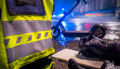 High visibility police vest and notebook in wet conditions near an electric scooter at night in the UK