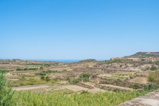 Agricultural fields with sea on the horizon between Gharb and Ghasri with chapel St. Dimitri and Ta' Gurdan lighthouse in the hills, Gozo MALTA