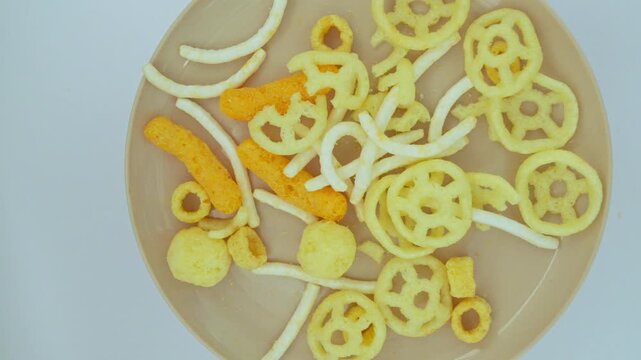 Top view of various unhealthy crunchy snacks pouring into a bowl isolated on a white background